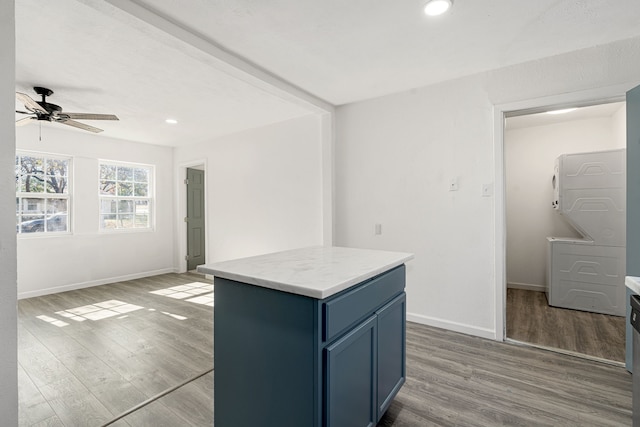 kitchen with stacked washer / dryer, a kitchen island, hardwood / wood-style floors, and ceiling fan