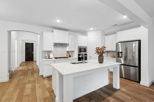 kitchen with appliances with stainless steel finishes, an island with sink, sink, white cabinets, and backsplash