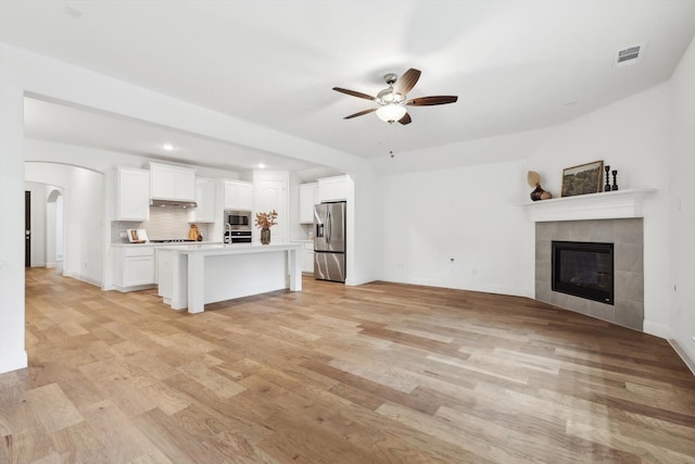 unfurnished living room featuring a tiled fireplace, ceiling fan, and light hardwood / wood-style flooring