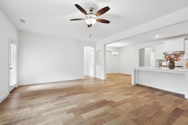 unfurnished living room with ceiling fan with notable chandelier and light hardwood / wood-style flooring