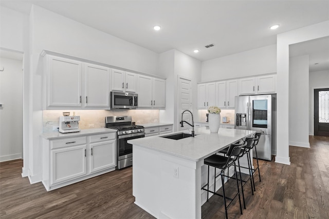 kitchen featuring stainless steel appliances, an island with sink, a kitchen bar, white cabinets, and sink