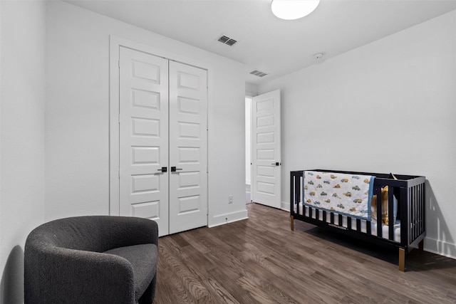 bedroom with a crib, dark hardwood / wood-style flooring, and a closet