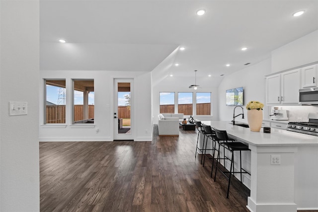 kitchen with a breakfast bar area, white cabinetry, a center island with sink, appliances with stainless steel finishes, and dark hardwood / wood-style flooring