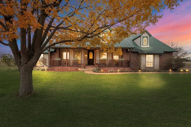 view of front of property featuring metal roof, a standing seam roof, a yard, a porch, and brick siding