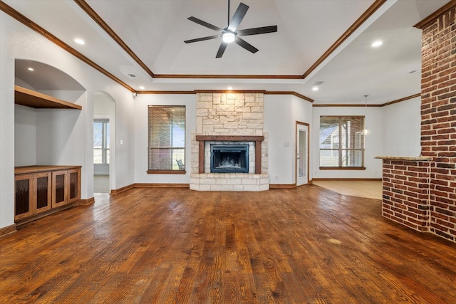 unfurnished living room with dark wood-type flooring, ceiling fan, crown molding, and a stone fireplace