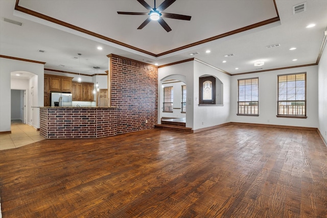 unfurnished living room with light wood finished floors, brick wall, visible vents, and arched walkways