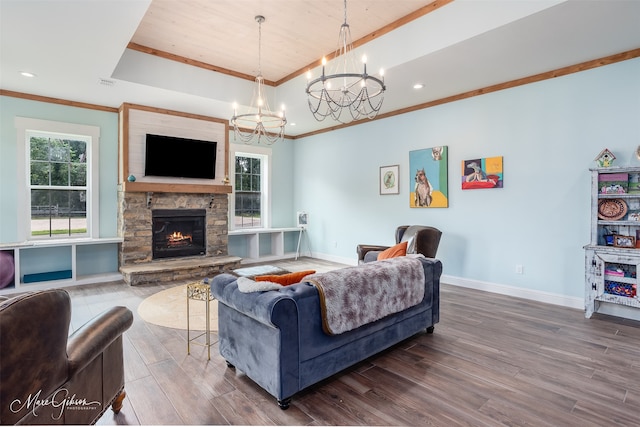 living room featuring a stone fireplace, crown molding, a chandelier, a tray ceiling, and hardwood / wood-style flooring