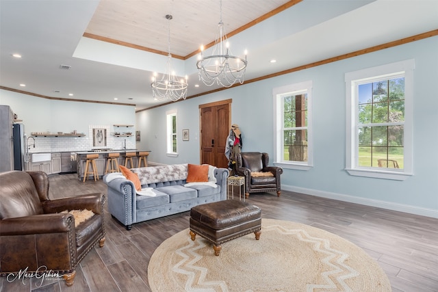 living room featuring ornamental molding, a raised ceiling, hardwood / wood-style floors, and a notable chandelier