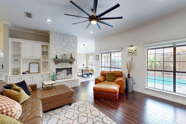 living room featuring crown molding, ceiling fan, a stone fireplace, and dark wood-type flooring