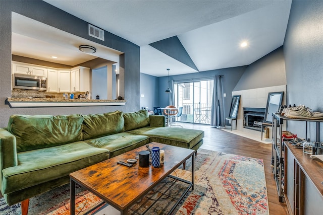 living room featuring wood-type flooring, vaulted ceiling, and a tiled fireplace