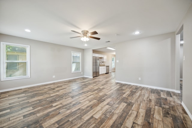 unfurnished living room featuring a wealth of natural light, dark wood-type flooring, and ceiling fan