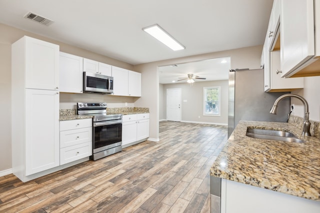 kitchen with light wood-type flooring, stainless steel appliances, white cabinetry, and sink