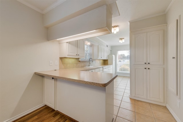 kitchen featuring backsplash, white cabinets, sink, ornamental molding, and kitchen peninsula