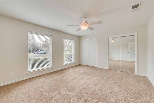 unfurnished bedroom with light carpet, ceiling fan, and multiple closets