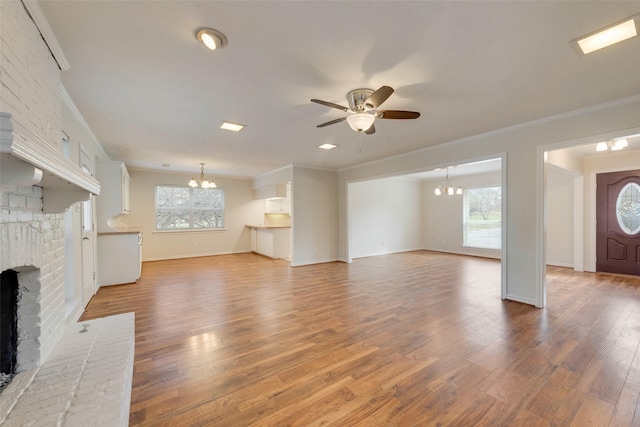 unfurnished living room featuring plenty of natural light, wood-type flooring, a fireplace, and ceiling fan with notable chandelier