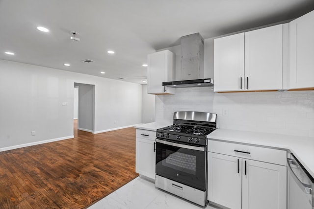 kitchen featuring wall chimney range hood, backsplash, light hardwood / wood-style floors, white cabinets, and appliances with stainless steel finishes