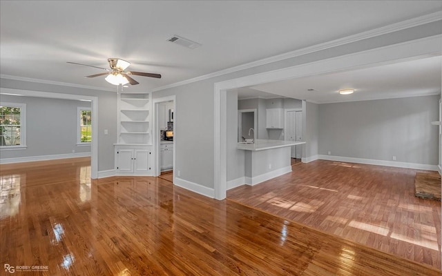 unfurnished living room featuring ceiling fan, sink, light wood-type flooring, and ornamental molding