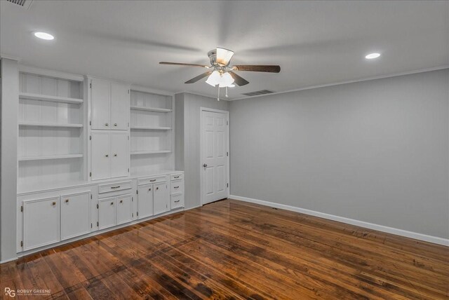 unfurnished living room with built in shelves, dark hardwood / wood-style flooring, ceiling fan, and crown molding