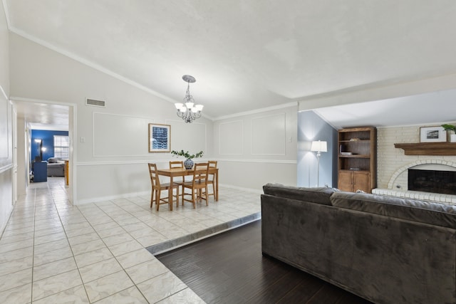 living room featuring an inviting chandelier, ornamental molding, vaulted ceiling, and a brick fireplace