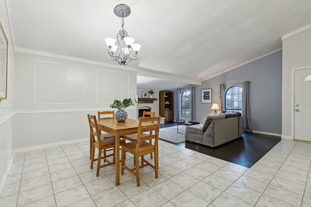 dining space featuring lofted ceiling, a large fireplace, crown molding, and a notable chandelier