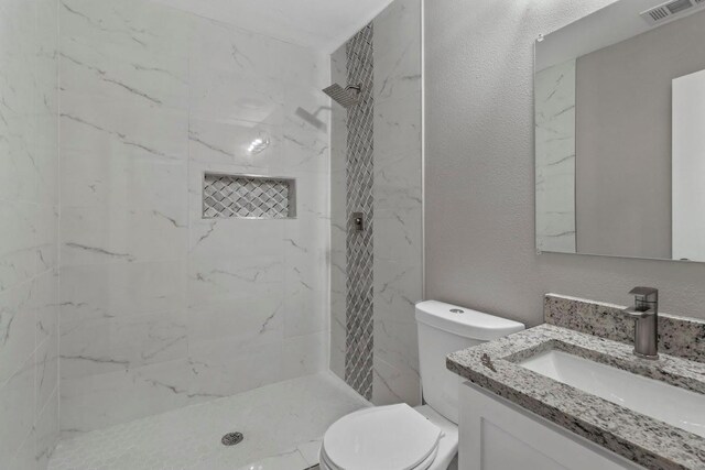 bathroom with tiled shower, vanity, and toilet