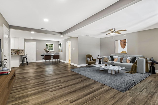 living room featuring beamed ceiling, ceiling fan, and dark wood-type flooring