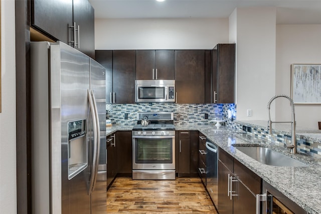 kitchen with dark brown cabinetry, light stone countertops, sink, light hardwood / wood-style floors, and appliances with stainless steel finishes