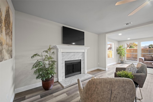 living room with a high end fireplace, hardwood / wood-style flooring, and ceiling fan