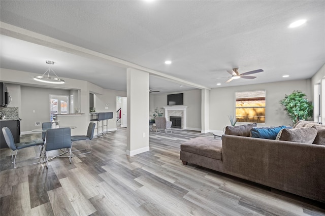 living room featuring ceiling fan, a high end fireplace, a textured ceiling, and light wood-type flooring