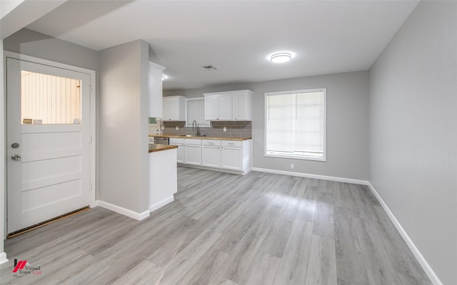 kitchen featuring white cabinetry, sink, tasteful backsplash, stainless steel dishwasher, and light wood-type flooring