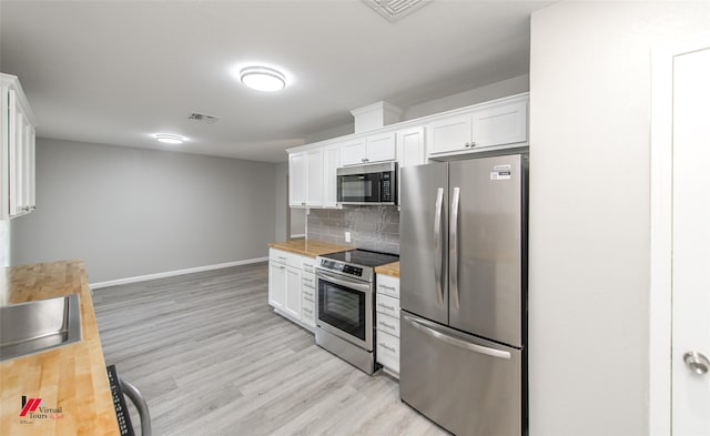 kitchen with appliances with stainless steel finishes, light wood-type flooring, backsplash, white cabinetry, and butcher block counters