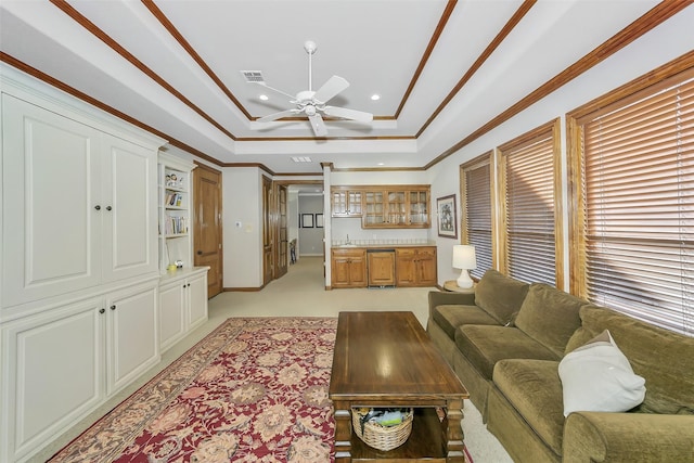 living room with a tray ceiling, crown molding, ceiling fan, and bar area