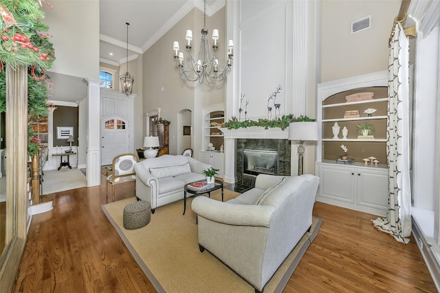 living room with hardwood / wood-style floors, a towering ceiling, an inviting chandelier, built in features, and crown molding