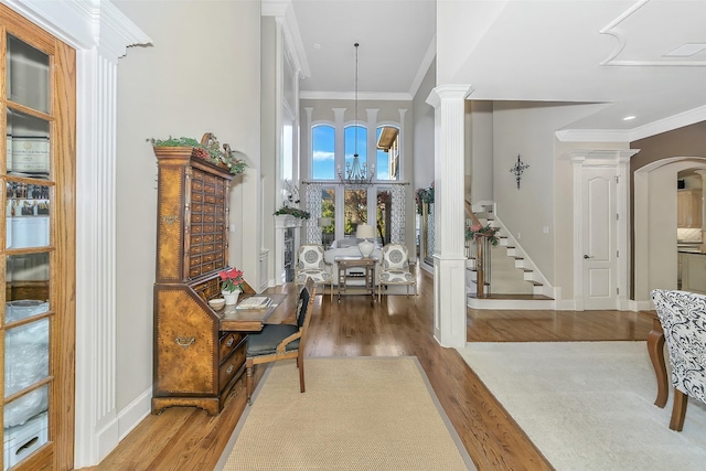 foyer entrance with crown molding, a chandelier, decorative columns, and hardwood / wood-style floors