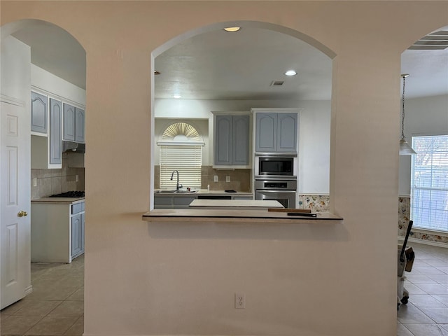 kitchen featuring kitchen peninsula, stainless steel appliances, sink, light tile patterned floors, and hanging light fixtures