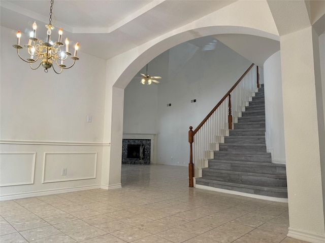 interior space featuring a high end fireplace, a towering ceiling, and ceiling fan with notable chandelier