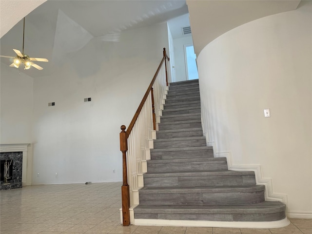 staircase featuring tile patterned flooring, high vaulted ceiling, ceiling fan, and a premium fireplace