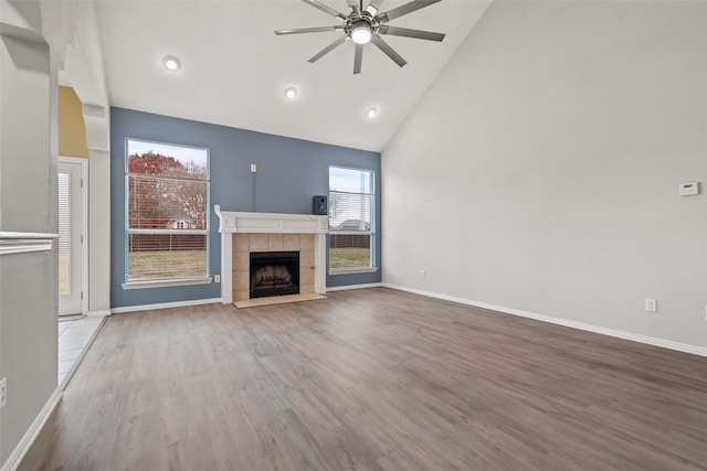 unfurnished living room featuring ceiling fan, wood-type flooring, a tiled fireplace, and high vaulted ceiling