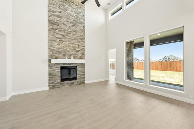 unfurnished living room featuring a towering ceiling, a ceiling fan, a stone fireplace, wood finished floors, and baseboards