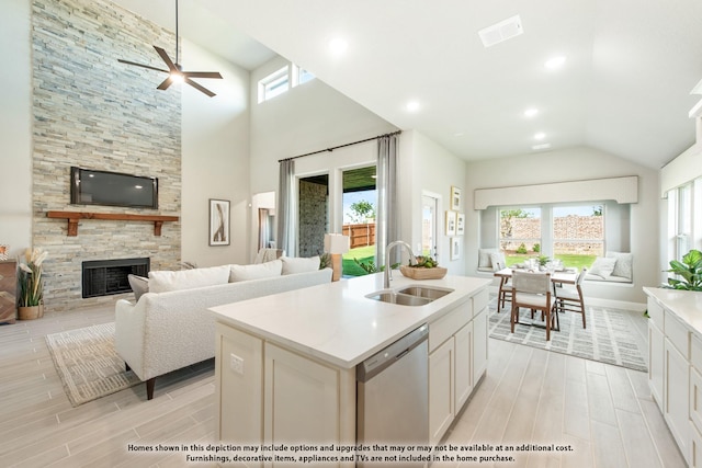 kitchen featuring sink, white cabinetry, a center island with sink, a stone fireplace, and stainless steel dishwasher