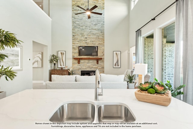 kitchen featuring ceiling fan, a fireplace, sink, and a high ceiling