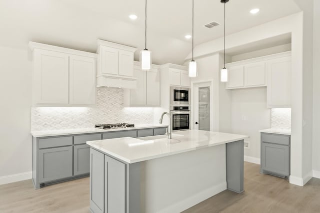 kitchen featuring visible vents, gray cabinets, a sink, stainless steel appliances, and decorative backsplash
