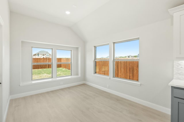 empty room featuring light wood-style flooring, vaulted ceiling, and baseboards