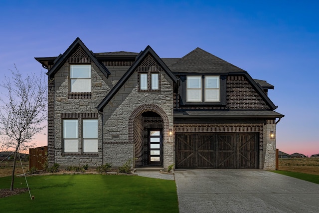 tudor-style house featuring roof with shingles, a front yard, stone siding, an attached garage, and concrete driveway
