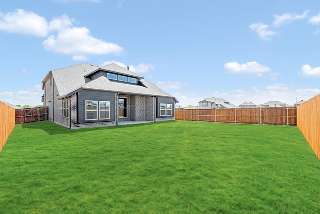 back of house with a yard, roof with shingles, a fenced backyard, and a patio area