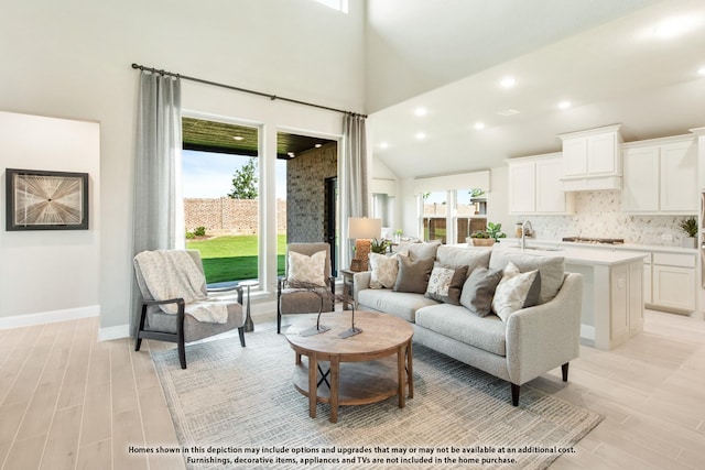 living room featuring a towering ceiling, plenty of natural light, sink, and light wood-type flooring