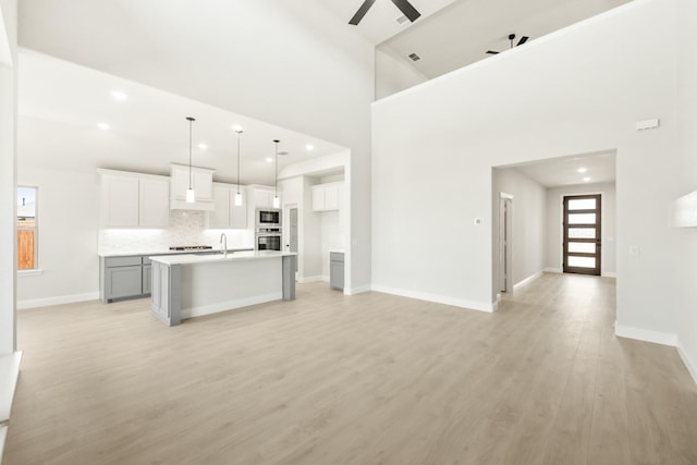 kitchen with oven, a ceiling fan, a center island with sink, backsplash, and built in microwave
