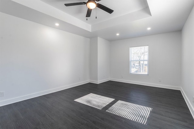 empty room featuring a raised ceiling, ceiling fan, and dark wood-type flooring