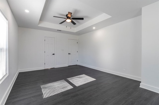 empty room featuring a tray ceiling, baseboards, dark wood finished floors, and a ceiling fan