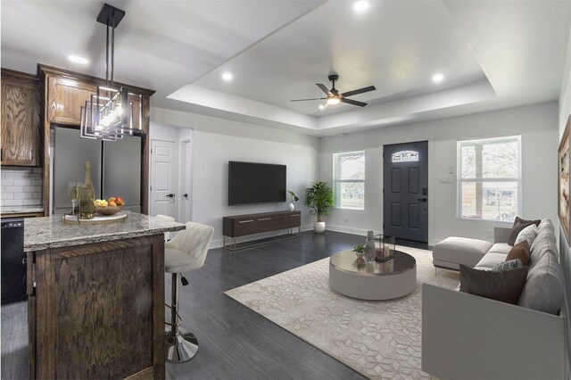 living room featuring dark hardwood / wood-style floors, ceiling fan, and a tray ceiling